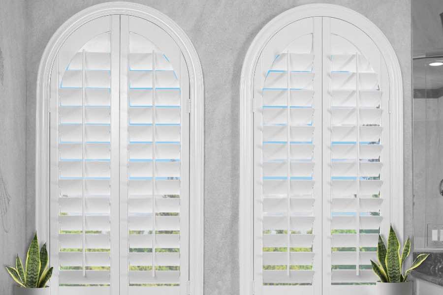 White Polywood shutters on two arched windows by a bathtub