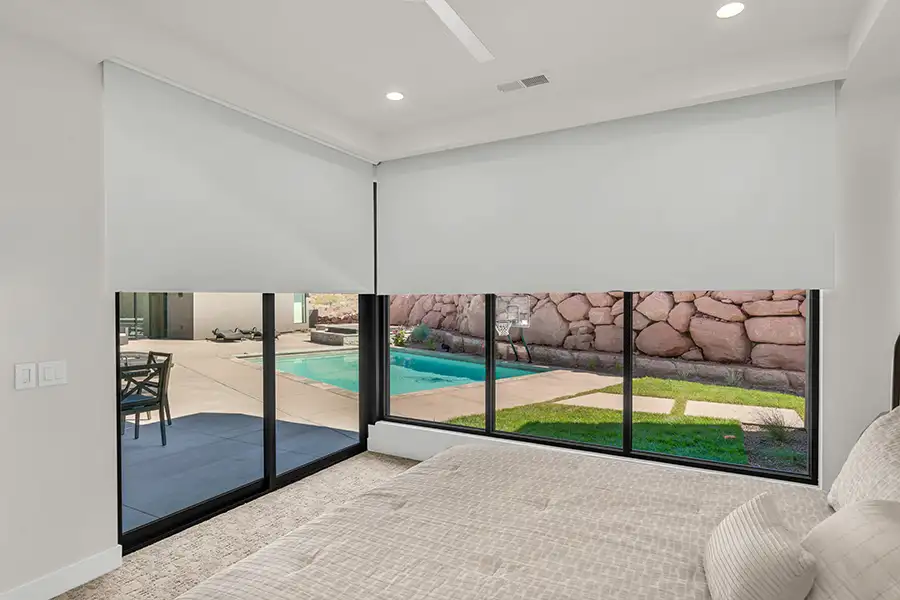 Install automatic shades that close by themselves before your house overheats each day. Large white shades on walls of windows in a bedroom overlooking a pool