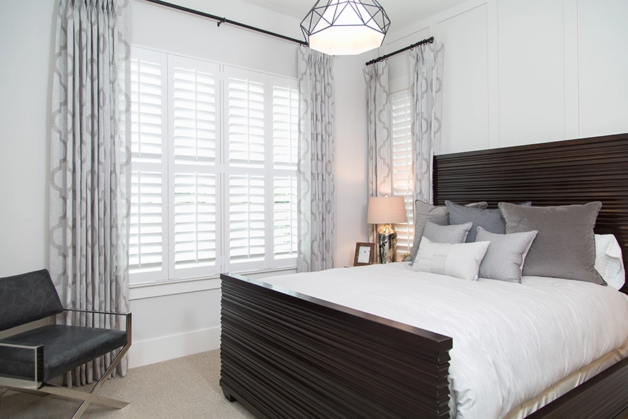 Unify diverse window sizes with sophisticated layered treatments and shutters. Mismatched bedroom windows with Polywood shutters and patterned curtains