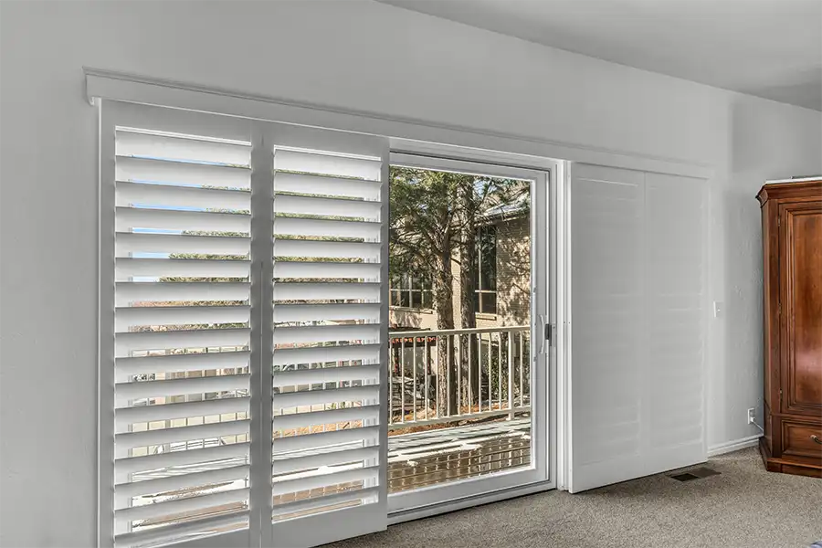 White plantation shutters covering a sliding door in a living room area